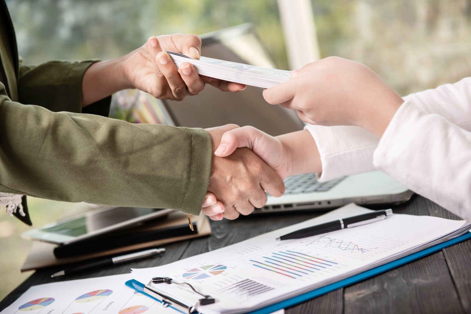 Business people shaking hands, finishing up meeting. businessman giving money to his partner while making contract - bribery and corruption concepts.